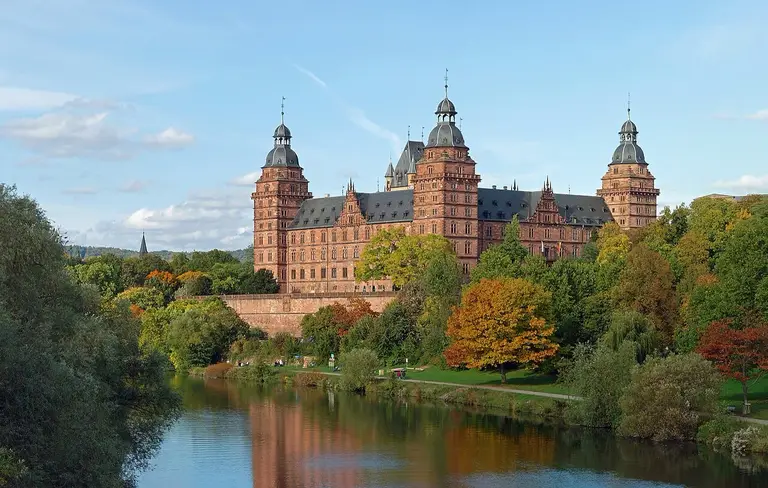 Das Renaissance-Schloss Johannisburg aus rotem Sandstein in Aschaffenburg mit seinen vier Ecktürmen unter blauem Himmel.