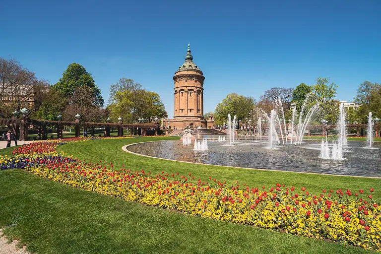Der historische Mannheimer Wasserturm aus rotem Sandstein im Jugendstil auf dem Friedrichsplatz, umgeben von Grünanlagen.