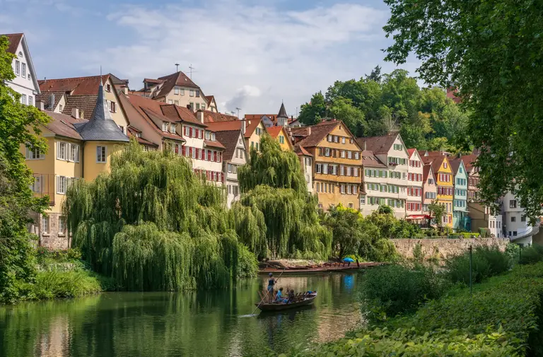 Die historische Neckarfront von Tübingen mit bunten Altstadthäusern und dem Hölderlinturm, davor ein Stocherkahn auf dem Neckar