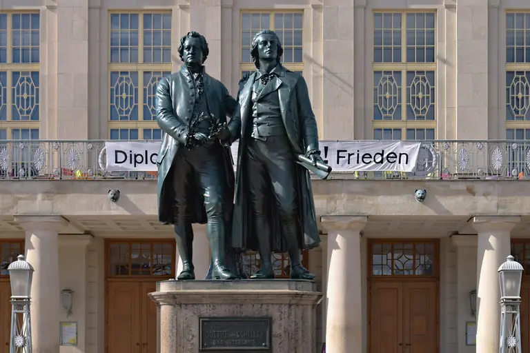 Das Goethe-Schiller-Denkmal auf dem Theaterplatz in Weimar, zwei Bronzefiguren der Dichter Goethe und Schiller auf einem Steinsockel.